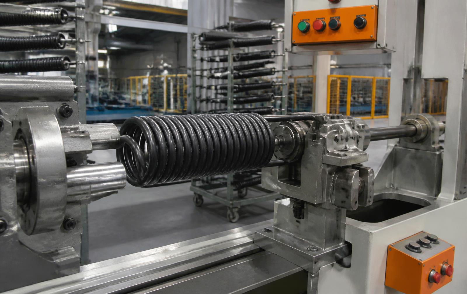 Black garage door torsion spring being formed on industrial coiling equipment